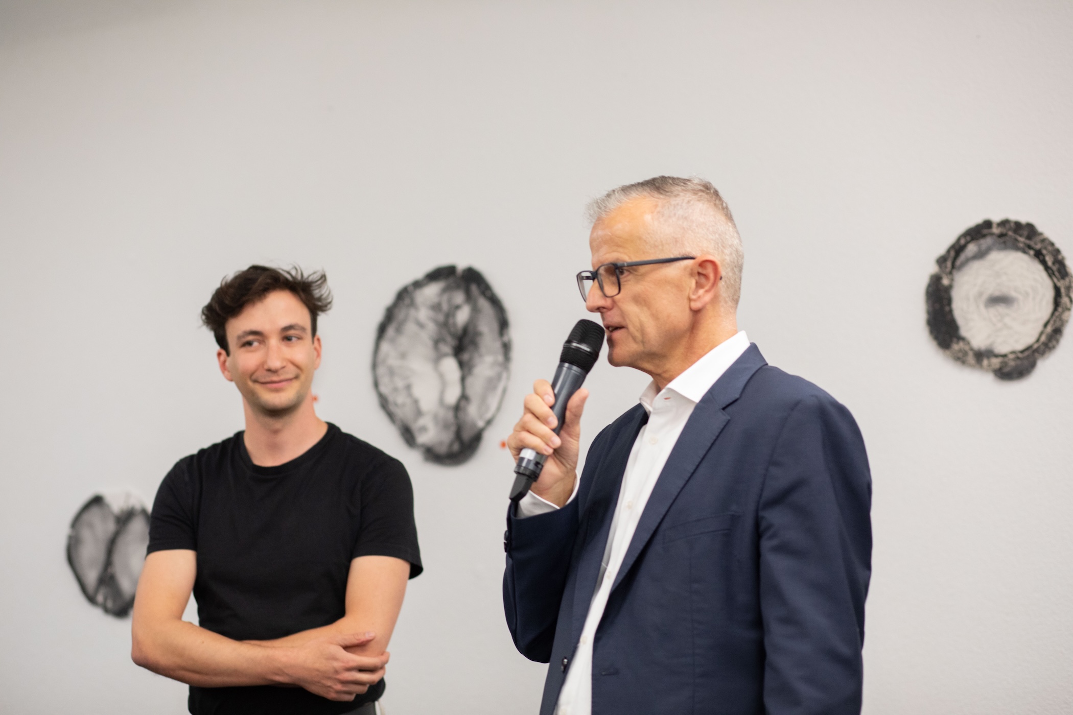 a@w_zürich_rede_mit_mikrofon_vor_kunstwerken a@w_zürich_rede_mit_mikrofon_vor_kunstwerken